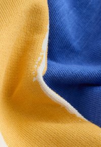 Katoenen stof in gedurfd geel en blauw met een contrasterende witte rand. De textuur lijkt glad en gebreid met een nette afwerking.