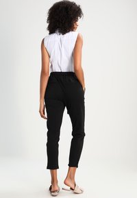 Pantalons noirs ajustés avec taille élastique et poches latérales, associés à un haut sans manches blanc, vus de l'arrière. Design simple.