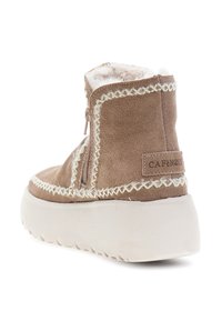 Bota de ante marrón claro hasta el tobillo con forro de piel sintética blanca, costuras decorativas blancas, cremallera lateral y suela de goma blanca gruesa.