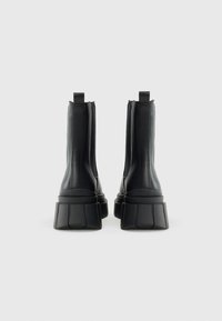 Black leather ankle boots with a chunky, textured sole and vertical stitching. Features a pull tab at the back for easy wear.
