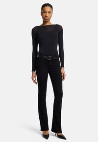 Svart langermet bodysuit med båtutringning, parret med svarte bootcut jeans og et teksturert svart belte. Svarte spissede hæler.