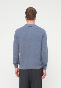 Blauer, langärmeliger Polopullover mit Kragen, der ein strukturiertes Strickmuster und gerippte Bündchen aufweist, von hinten betrachtet.