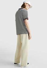 Polo a righe in blu navy e crema con maniche corte, abbinato a pantaloni larghi beige e sneakers bianche, visto da dietro.