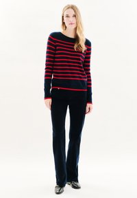 Gestreifter Pullover in Marineblau und Rot mit einem Bootsausschnitt, kombiniert mit dunkelblauen, weiten Hosen und schwarzen Schuhen. Weicher Stoff, lässiges Design.