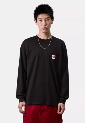 Camisa negra de manga larga con un bolsillo en el pecho que presenta un logotipo de corazón blanco y rojo. Cuello redondo, corte relajado, textura suave.