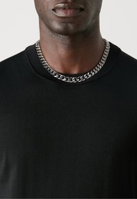 Suéter negro de cuello redondo hecho de tela texturizada, con un collar de cadena de metal plateado alrededor del cuello.