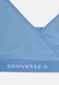 Ljust blå bomullsbehå med V-ringning, med en mjuk textur och en logoband med texten "CONVERSE" i vitt.