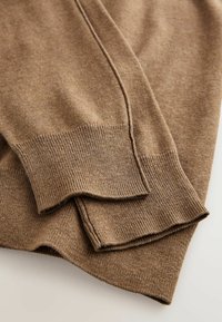 Bruine gebreide trui met geribde manchetten, met een zachte textuur en subtiele stikseldetails. De stof lijkt lichtgewicht en flexibel.
