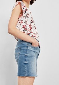 Halenka s květinovým vzorem ve světle růžové barvě s volánovými rukávy, spárovaná se světle modrými džínovými šortkami s třepeným lemem a mírným opotřebením.