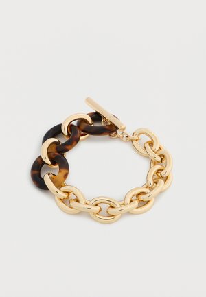 Zlatna narukvica s izmjeničnim ovalnim poveznicama od školjke kornjače i zlata te zlatnim preklopnim kopčom na bijeloj pozadini.