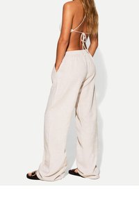 Beige linnebyxor med vida ben, elastisk midja och sidofickor. Matchas med svarta sandaler med rund guldfärgad detalj.