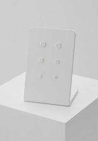 Biely štvorcový podstavec s zaoblenými rohmi, so štyrmi vyvýšenými kruhovými bodkami usporiadanými vertikálne. Hladký povrch, minimalistický dizajn.