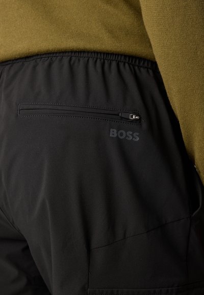 Черни платнени панталони с еластичен пояс, с къс гръб с цип и логото "BOSS" в дискретен матов завършек.