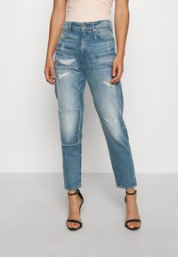 Světle modré ošuntělé džíny s volným střihem, zdobené vsadkami a roztrhanými lemy. Nosené s černými páskovými podpatky.