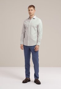 Camicia button-up grigia chiara con una texture liscia, abbinata a pantaloni blu a righe verticali. Il modello indossa mocassini scuri su uno sfondo neutro.