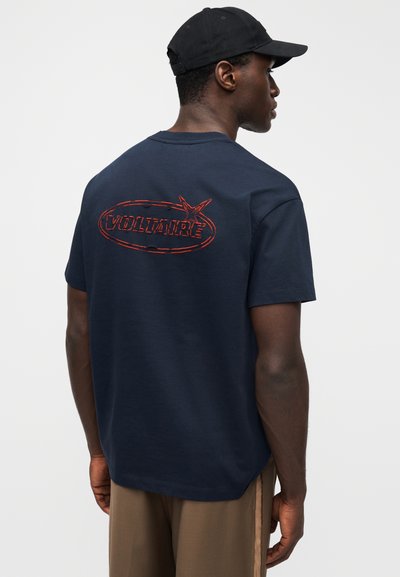 Tmavě modré bavlněné tričko s �červeným vyšívaným logem „VOLTAIRE“ na zádech. Krátké rukávy, volný střih a kulatý výstřih.