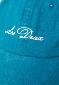 Teal baseball cap with white cursive embroidery reading "Les Deux" on the front panel.