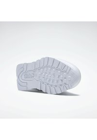 Suela de zapatilla de goma blanca con patrones de agarre texturizados, bordes estriados y la marca Reebok, diseñada para ofrecer tracción y durabilidad.
