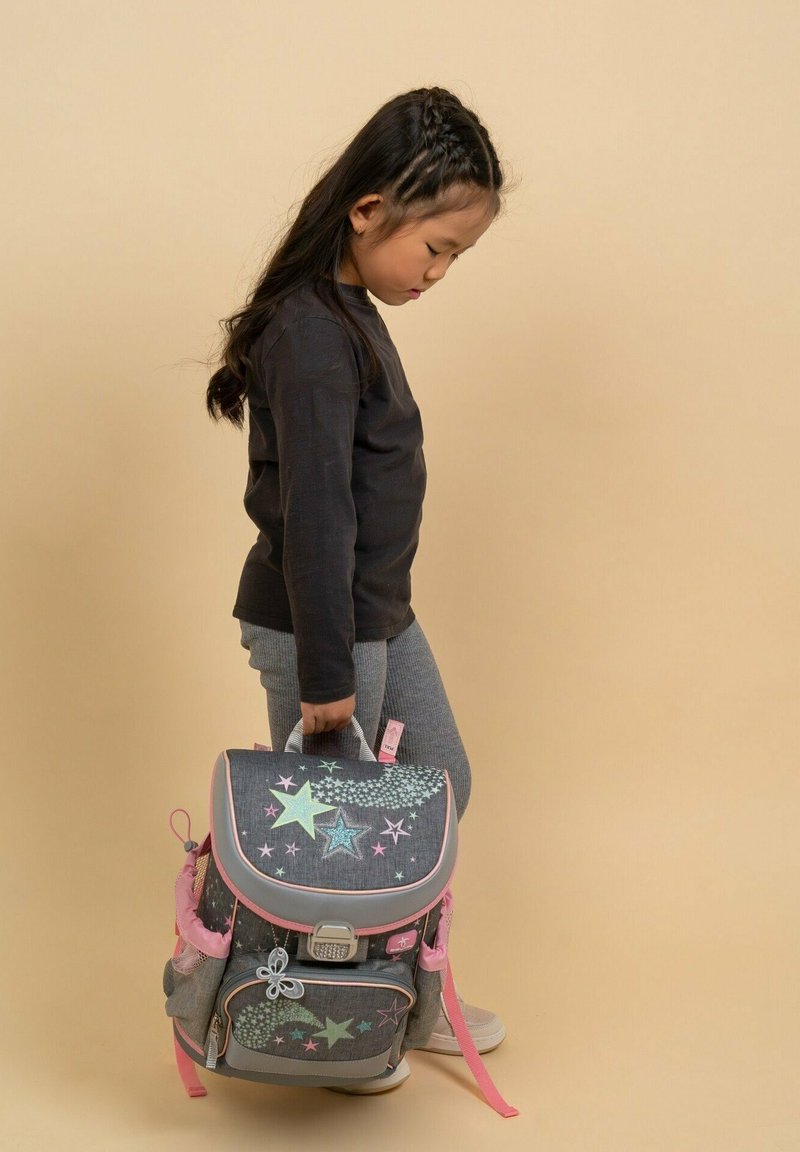 Grauer Denim-Rucksack mit pastellfarbenen Sternmustern, rosa Akzenten, einer Fronttasche und einem oberen Griff; ein Kind hält ihn am Griff.