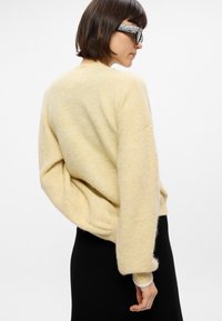 Pull en maille jaune clair avec une coupe décontractée, des épaules tombantes et des poignets côtelés. Texture douce, porté avec une jupe noire.