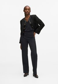 Fekete, rövidített fazonú dzseki arany gombokkal, sötét nadrággal párosítva. Az öltözék sima anyaggal rendelkezik és testhezálló fazonú. Fekete, díszített cipőkkel.