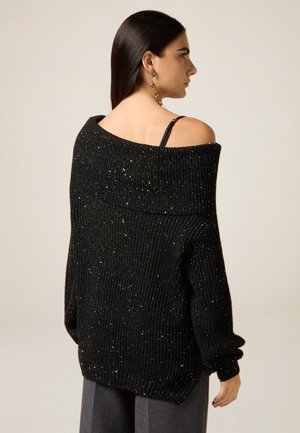 Maglione nero a coste con design scollato sulle spalle e scintillii metallici, con maniche ampie e una texture accogliente.