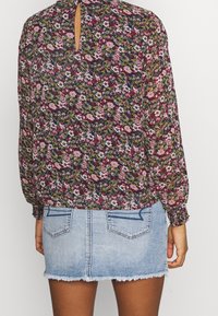 Blommig långärmad blus i mörka färger med nyckelhål på ryggen, kombinerad med en ljus denim minikjol med fransad nederkant och två bakfickor.