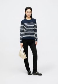 Maglione a righe navy e bianche con maniche lunghe, abbinato a jeans neri slim-fit e scarpe nere. Borsa beige con dettagli dorati.