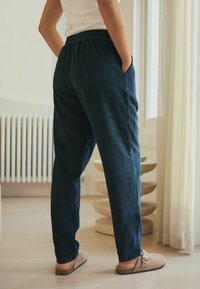 Pantalones de pana azul marino con una cintura elástica, bolsillos laterales y un diseño de pierna ajustada; llevados con zapatos tipo mocasín de color marrón claro.