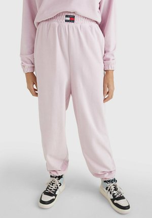 Pantaloni della tuta rosa chiaro con vita e polsini elastici, con etichetta del logo Tommy Jeans. Abbinati a sneakers alte bianche e nere.