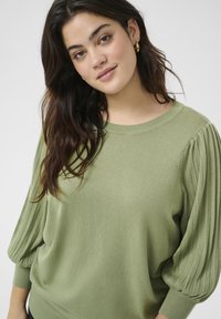 Hellgrüner gestrickter Pullover mit leicht gepufften Ärmeln, gerippten Bündchen und rundem Halsausschnitt. Weiche Textur mit lässigem Schnitt.