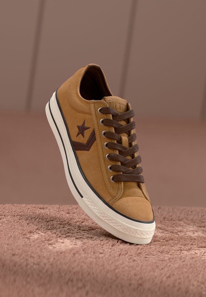 Beżowe zamszowe sneakersy z brązowymi sznurówkami, gwiazdą na detalu, białą podeszwą środkową i teksturowaną powierzchnią. Posiadają klasyczny okrągły czubek i wzmocnione szwy.