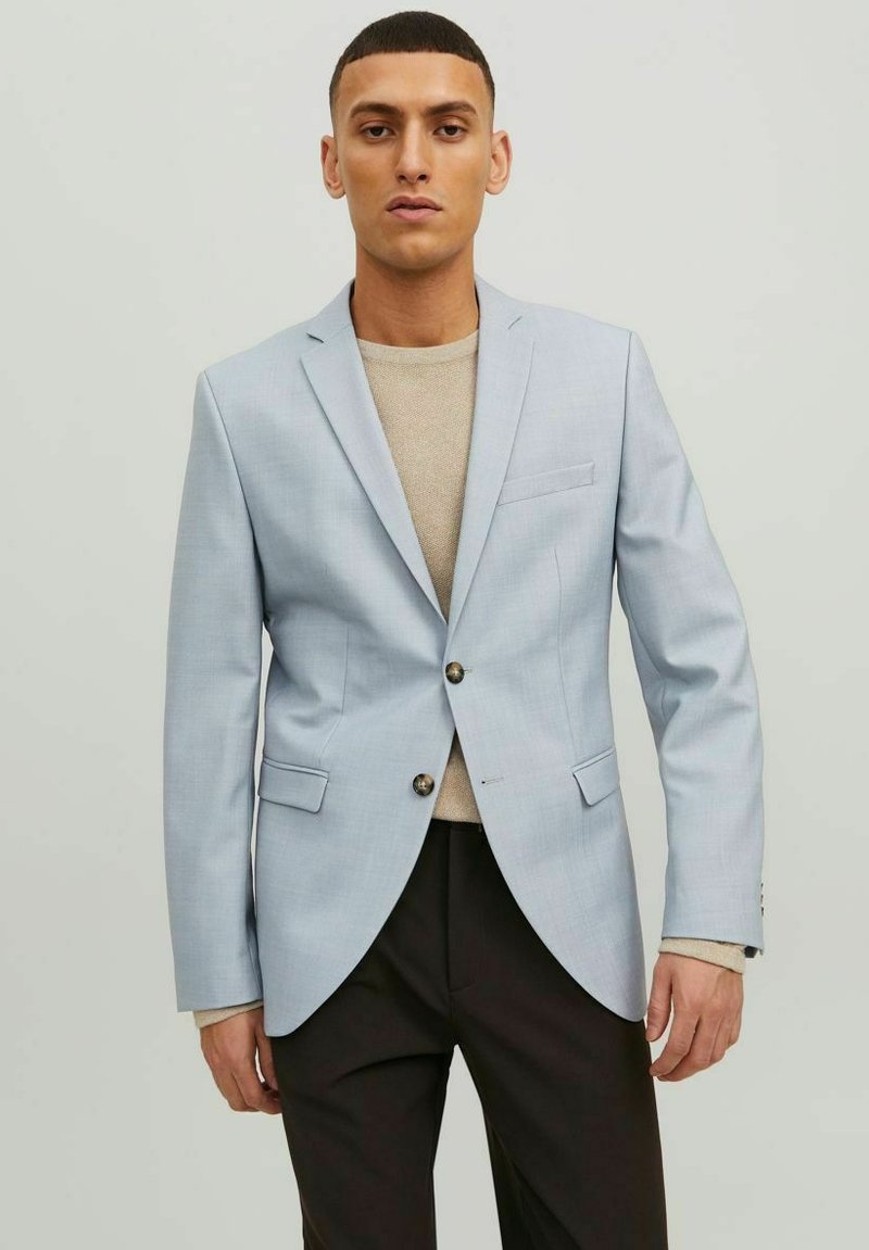 Blazer su misura azzurro chiaro con risvolti, due tasche frontali, chiusura con un bottone e trama liscia, indossato sopra un maglione beige lavorato a maglia.