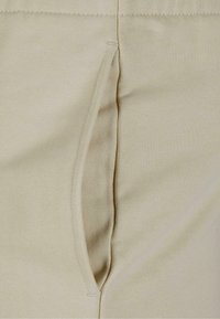Beige sporta bikses ar sānu kabatu un ribotu tekstūru. Audums ir mīksts ar gludu apdari un minimālu šuvju detalizāciju.