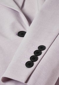 Liliowy materiałowy żakiet z rękawami, pięcioma czarnymi guzikami i fioletowymi przeszyciami. Gładka tekstura z subtelnym wzorem tkanym.