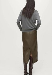Pull gris et jupe en cuir vert olive avec une fente à l'arrière, associée à des bottes marron brillantes, vue de dos.
