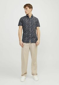 Camicia a maniche corte floreale in blu navy con piccoli fiori multicolori. Tessuto morbido, design con colletto, chiusura frontale a bottoni, abbinata a pantaloni beige.