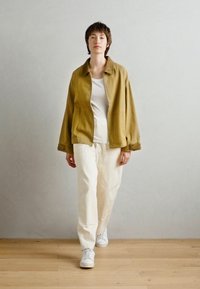 Tan, oversized jacket in soft fabric with a collar, paired with a white T-shirt and cream trousers. White sneakers complete the outfit.