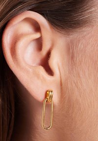 Gouden oorbellen in de vorm van hoepels met een schakeldesign, voorzien van gladde oppervlakken en een glanzende afwerking, hangend aan een doorboorde oorlel.