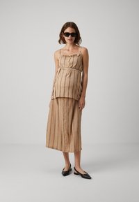 Beige stripet kjole med tettsittende overdel, volang hals, knappestolpe foran og en luftig skjørt. Brukt med svarte spisse flate sko.
