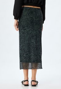 Zwarte en donkergroene luipaardprint midi-jurk met een transparante textuur, elastische tailleband en een rechte snit, gecombineerd met zwarte sandalen.