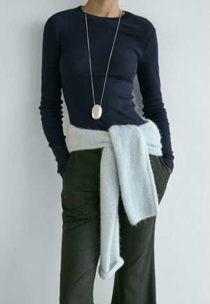 Maglia a maniche lunghe color blu navy, fascia in maglia azzurro chiaro annodata in vita e pantaloni a righe scure. Collana con ciondolo d'argento che aggiunge un tocco metallico.