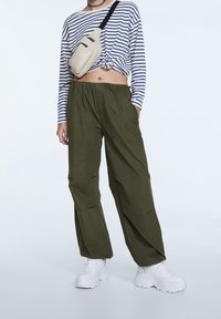 Pantalon cargo vert, ample, avec une taille élastique et des poches latérales, associé à une chemise à manches longues rayée bleu et blanc.