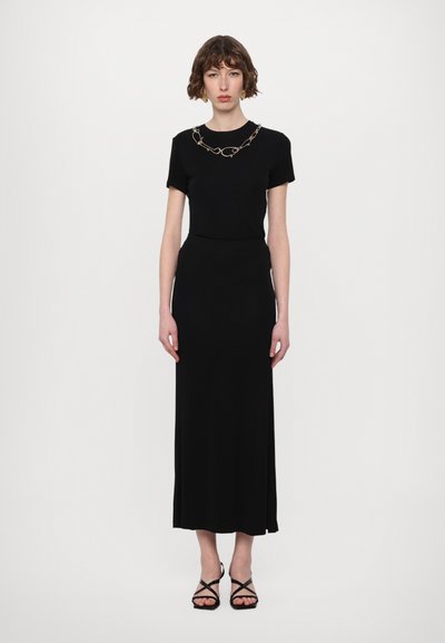 Black, fitted dress with short sleeves, textured fabric, and ankle-length skirt. Accented with a gold chain necklace. Strappy black sandals.