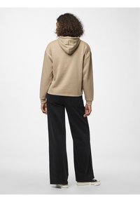 Felpa beige con tasca a canguro e cappuccio con cordino, abbinata a pantaloni neri a gamba larga. Il tessuto è morbido e ha una vestibilità comoda.