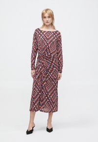 Dlouhé, vzorované šaty s geometrickým designem v červené, modré a bílé barvě. Vyrobené z lehkého materiálu, s volným střihem a dlouhými rukávy.