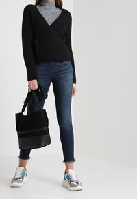 Czarny dzianinowy sweter w oversize'owym fasonie na szarym golfie, połączony z ciemnymi dżinsami, czarną torebką ze zamszu oraz wielokolorowymi sportowymi butami.