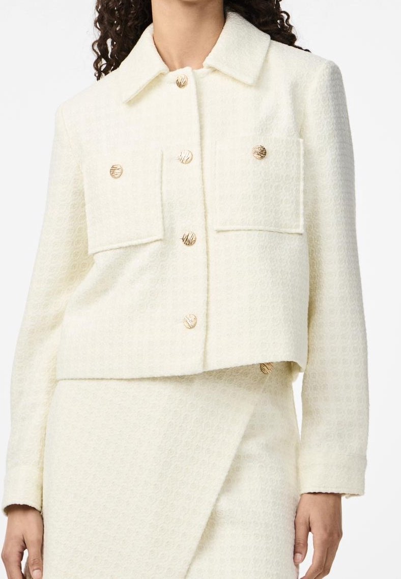 Femme portant une veste écrue texturée avec des boutons dorés et une jupe assortie avec un panneau avant superposé.