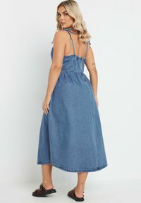 Denim midi-mekko, jossa on säädettävät olkaimet, kiristettävä vyötärö ja levenevä helma. Vaaleansininen väri ja sileä rakenne.
