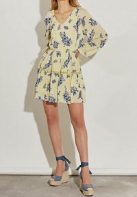 Vestido floral amarillo con patrones azules, escote en V, cintura elástica y falda en capas. Combinado con cuñas de esparto azules y lazos de cinta.